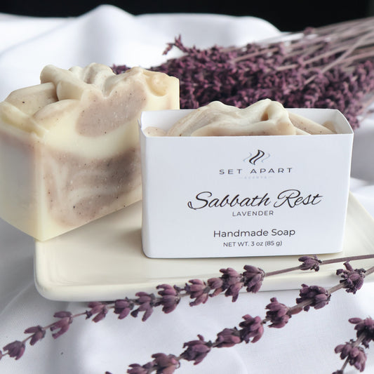 Bar of soap with a white label featuring text, surrounded by lavender flowers.